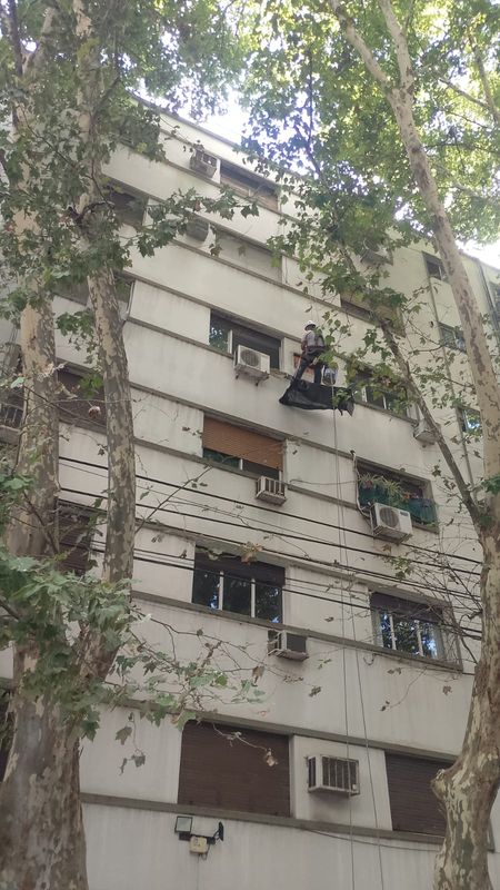 Técnico suspendido con cuerdas en fachada de edificio residencial retirando un equipo de aire acondicionado