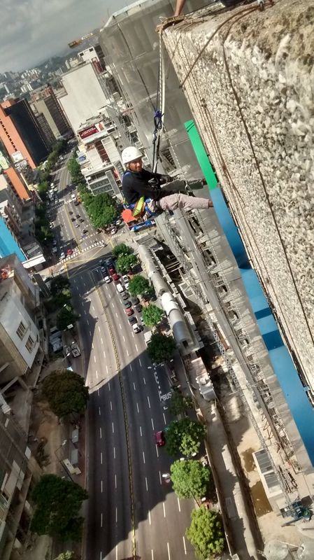 Técnico en acceso por cuerdas trabajando sobre fachada de edificio alto con vista a la avenida