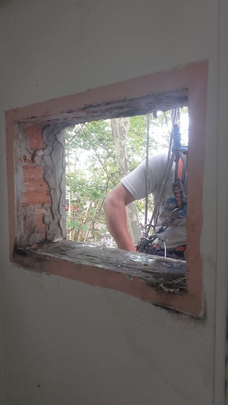 Técnico en cuerdas retirando un equipo de climatización a través de un vano en fachada