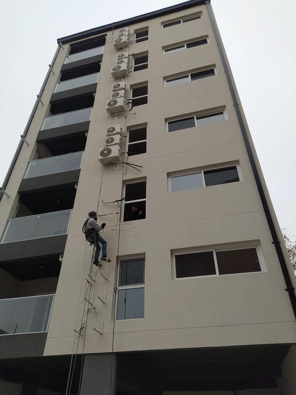 Técnico en acceso por cuerdas instalando unidades de aire acondicionado en fachada de edificio