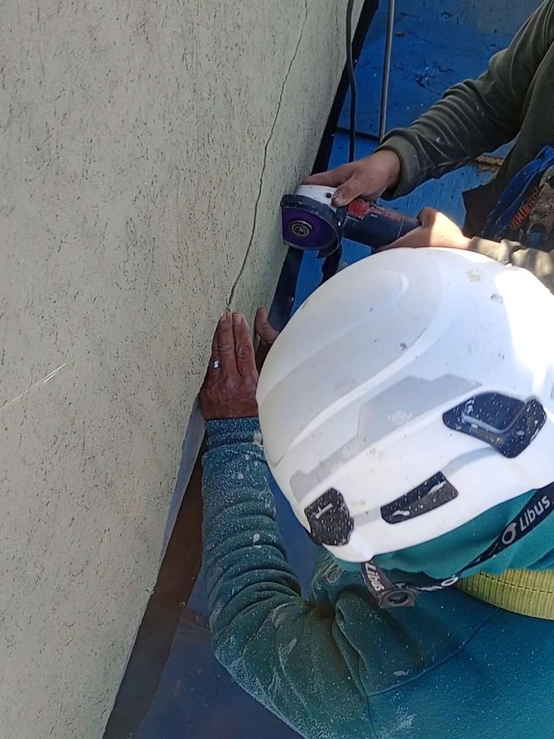 Técnico con casco y arnés haciendo un corte controlado con amoladora sobre la fisura del frente de un balcón