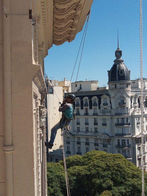 Técnico en acceso por cuerdas sobre fachada patrimonial de Avenida de Mayo, con cúpula al fondo