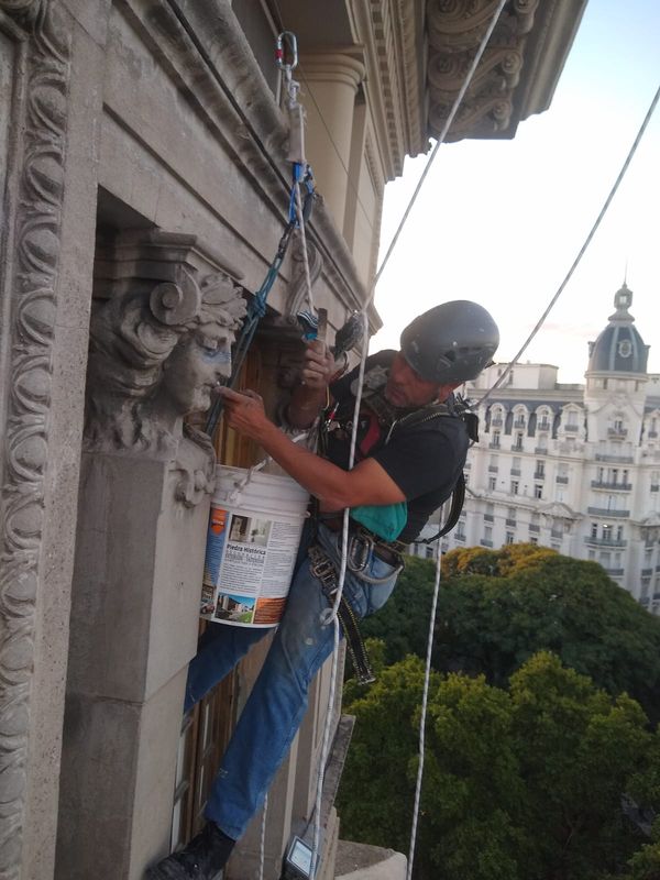 Técnico suspendido con cuerdas junto a ornamentos de fachada patrimonial en Avenida de Mayo