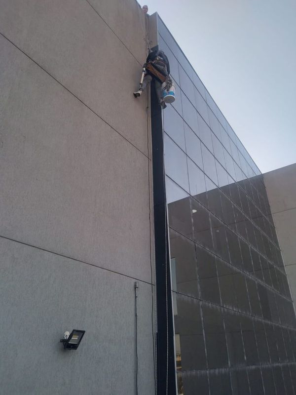 Técnico en acceso por cuerdas sellando juntas en fachada vidriada de un edificio en CABA